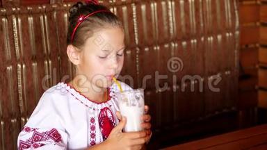 快乐的微笑少女孩子在咖啡馆喝奶昔。 她穿着乌克兰民族服装，刺绣